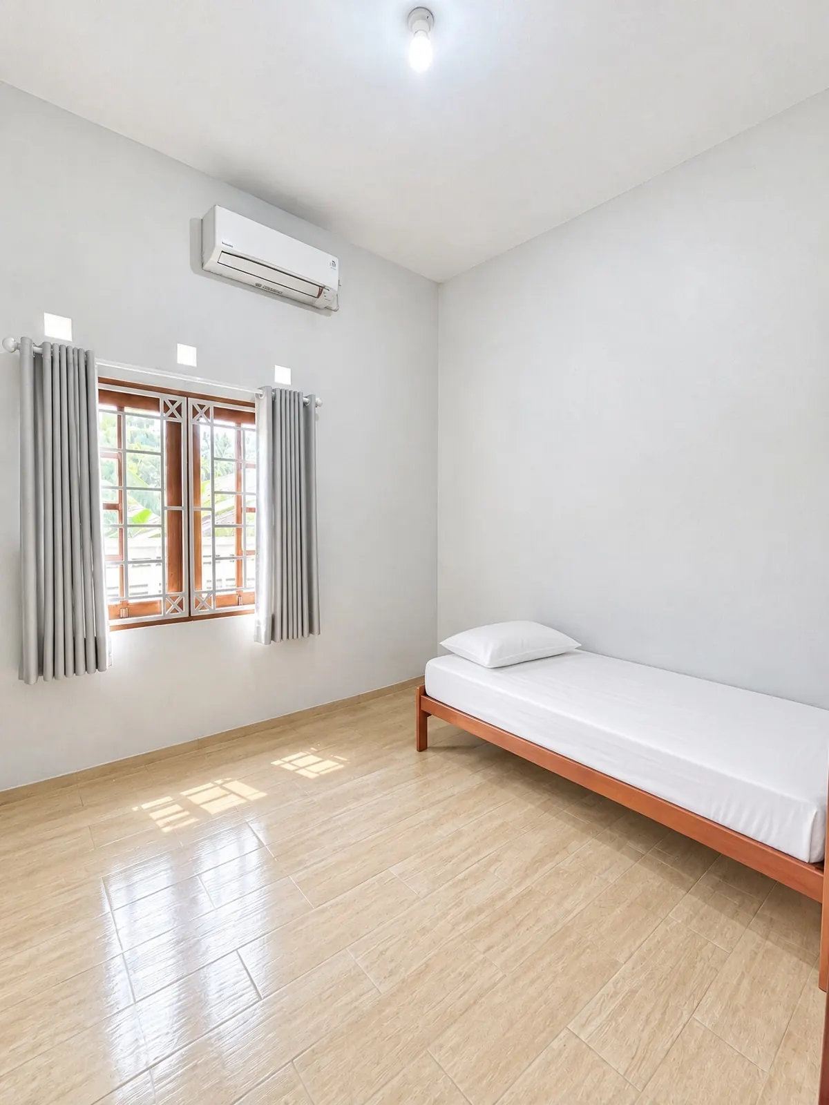 Bright single room with an air conditioner, a window with curtains and a single bed