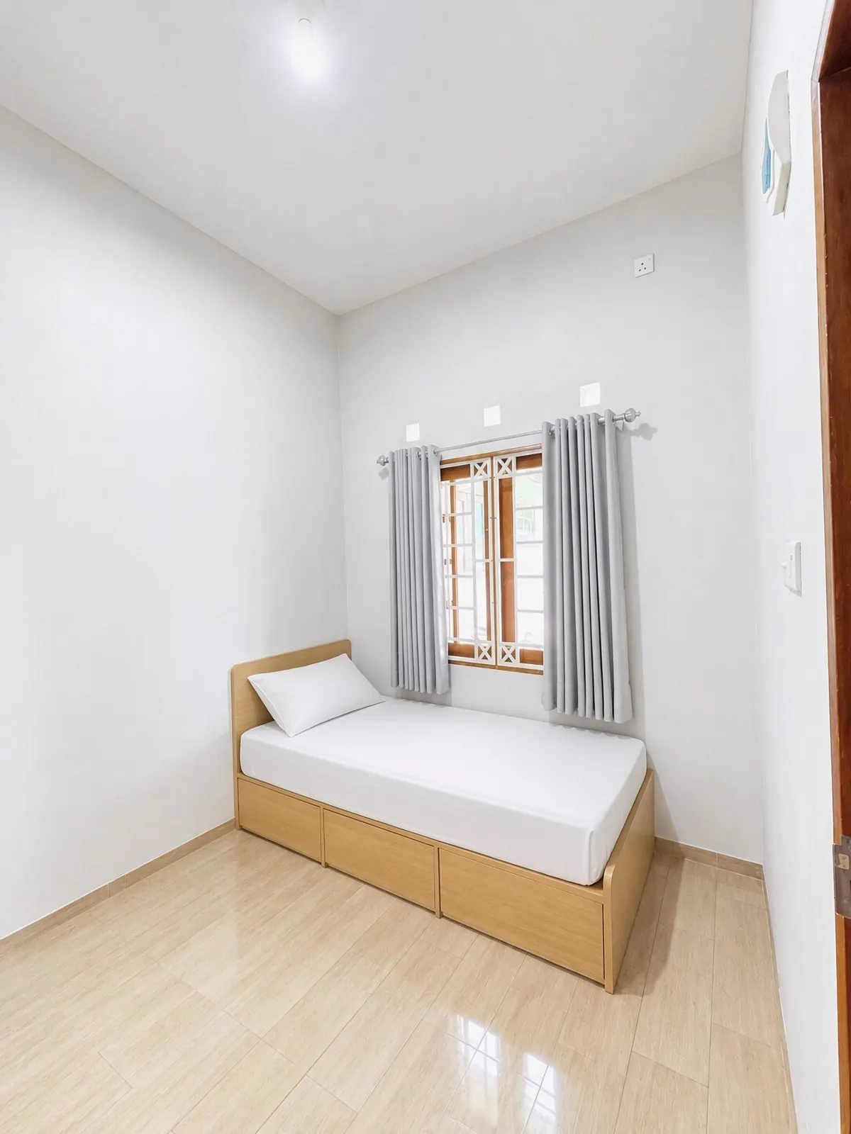 Single room with a bed that has storage drawers underneath and a window with curtains